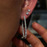 Close-up of an ear with multiple diamond earrings and a hand holding the ear.