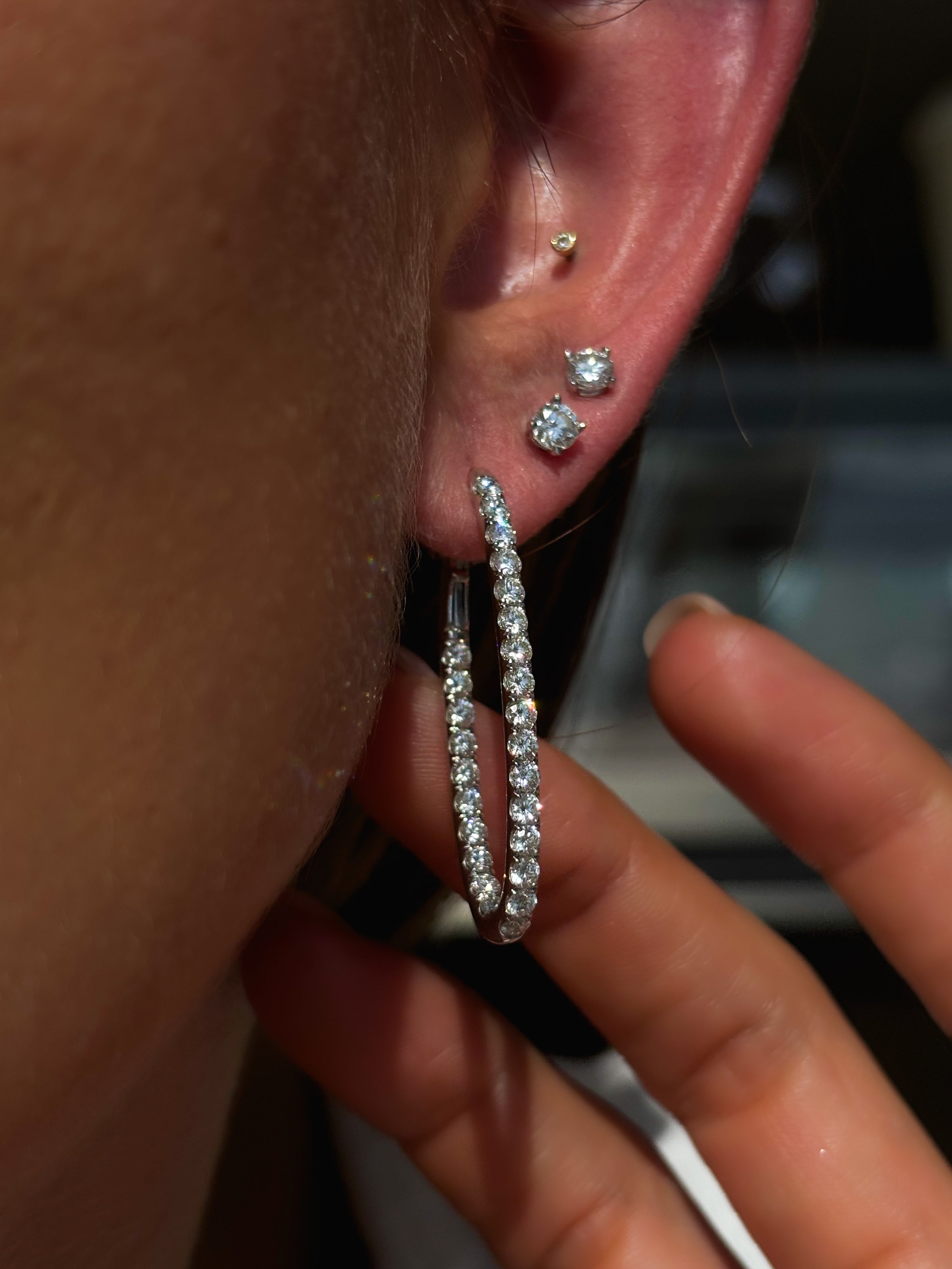 Close-up of an ear with multiple diamond earrings and a hand holding the ear.
